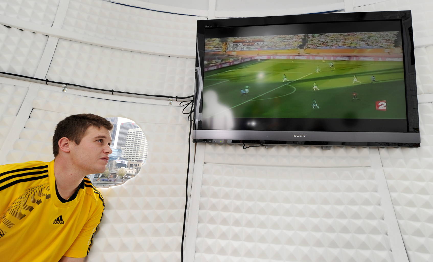 Competition winner Adam Santarossa watches the TV screen as he spends 31 days in a giant replica Jabulani World Cup ball, watching all 64 games from South Africa, in Melbourne on June 23, 2010.  Santarossa has to spend a minimum of 22 hours a day in the ball, only been allowed out for toilet breaks, food and a bit of excercise.  The giant Jabulani, which is a bit harder to kick than the real ball, weighs in at two tonnes, is 6m high and 6m wide, a scale of 30:1 over the actual Jabulani, and is Santarossa home for the World Cup and where he spends his spare time doing daily blogs and match reports after every match.  AFP PHOTO/William WEST (Photo credit should read WILLIAM WEST/AFP via Getty Images)